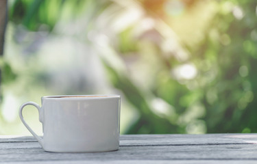 Hot coffee cup with white the wooden table and the Green leaf background with copy space on right