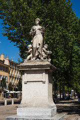 Fototapeta na wymiar Stone feminin statue on the famous Aix-en-Provence street cours Mirabeau surrounded by green trees. France 2019.