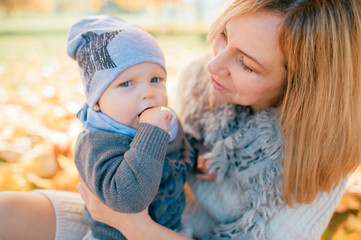 Mother holding her lovely son on her knees in autumn park.