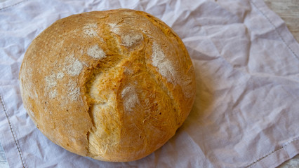 Top view on rustic bread on a natural linen napkin background. Home baked bread isolated on natural textured background. Round home-made bread. Fresh bakery image with copy space for your text.