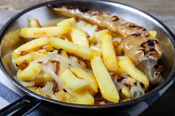 Delicious roast potatoes with onion and spices in a pan on kitchen towel on the old wooden table. Traditional rural dinner