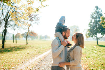 Fototapeta premium Family couple posing outdoor with their baby sitting on fathers shoulders