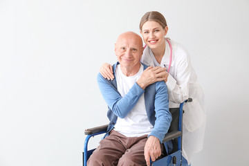 Elderly man with doctor on light background