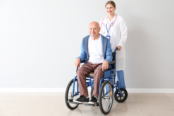Elderly man in wheelchair and doctor near light wall