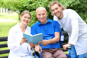 Elderly man with caregivers reading book in park