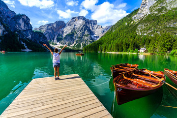 Woman relaxing on Pier at Lake Braies also known as Pragser Wildsee  in beautiful mountain scenery. Amazing Travel destination Lago di Braies in Dolomites, South Tyrol, Italy, Europe. - obrazy, fototapety, plakaty