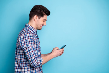 Side profile half turned photo portrait of confident positive optimistic excited involved interested carefree generation y guy holding digital telephone in hand leaving share post isolated background