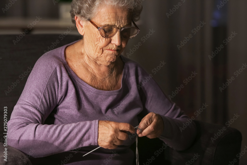 Wall mural senior woman knitting at home late in evening