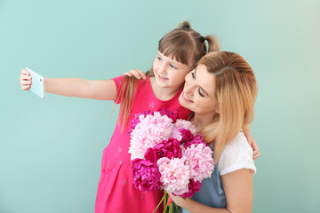 Little girl and her mother taking selfie with flowers on color background