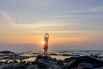 Calm young woman standing on the background of the sea and expressing joy. Female posing against wonderful sunset in the last rays of the sun.