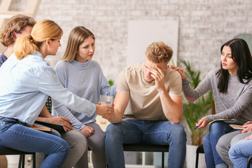 People calming depressed man at group therapy session