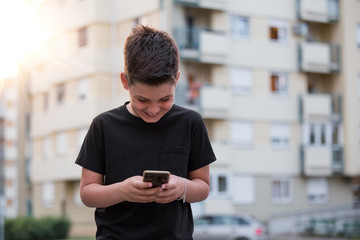 Teenage boy smiling while texting his friends via social networks using mobile phone, sitting against urban landscape background