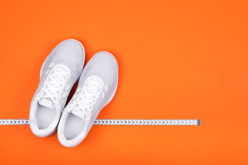 White sport shoes (sneakers) with measuring tape on bright russet orange background. 