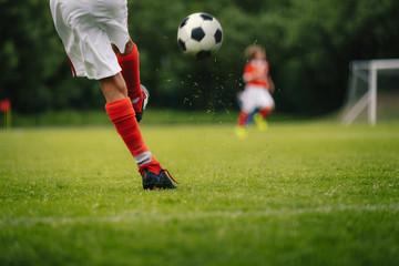 Football Kick. Youth Player Kicking Soccer Ball on Field. Football Ball in Motion. Legs of Sports Soccer Football Player Sportsman In Motion With Ball