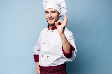Positive professional happy man chef showing tasty ok sign isolated on light blue.