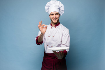 Positive professional happy man chef showing tasty ok sign isolated on light blue.