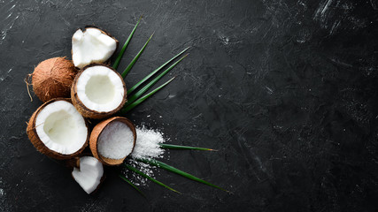 Coconut with palm leaves on a black stone background. Tropical Fruits. Nut. Top view. Free space for your text.