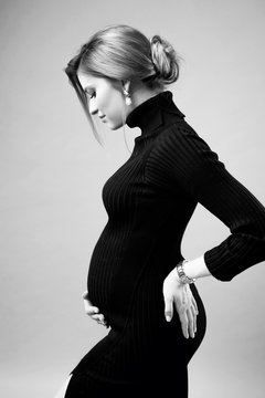 Young elegant pregnant woman with one hand on the lower back, the other under the tummy. Profile view.