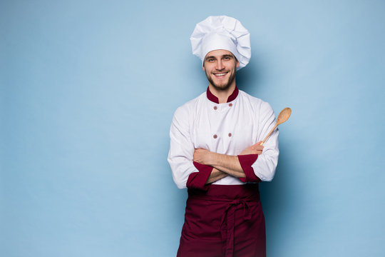 Portrait of positive toothy chef cook in beret, white outfit having tools in crossed arms looking at camera.