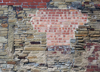 large old wall made of mixed bricks and stone with many jumbled patched and uneven repairs