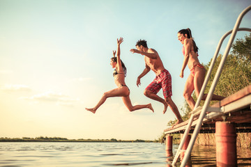 A group of young people joyfully leap into the refreshing lake waters on a sunny summer day,...