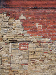 a full frame image of a large old wall made of mixed bricks and stone with many patched and uneven repairs