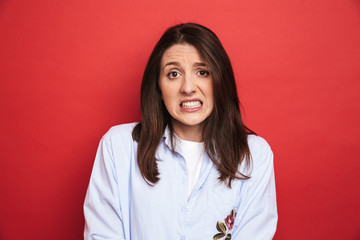Fototapeta premium Amazing confused young beautiful woman posing isolated over red wall background.
