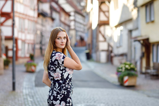 Beautiful young woman with long hairs in summer dress going for a walk in German city. Happy girl enjoying walking in cute small fachwerk town with old houses in Germany.