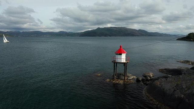 Powerful Cinematic Rotating Aerial of Small Lighthouse in Norwegian Fjord in North Sea With Sailing Boat and Green Coastline