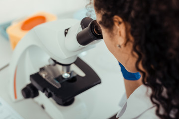 Top view of a dark haired woman looking into the microscope