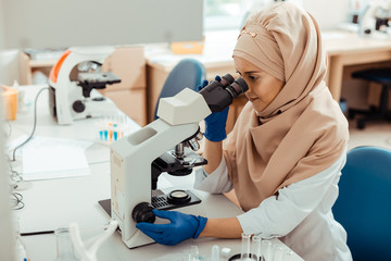 Intelligent muslim woman using the microscope for work