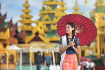 Burmese girl holding a red umbrella walking at Shwedagon Pagoda. Young Myanmar girls with Thanaka, a yellowish-white paste made from ground bark and used as a cosmetic and for sunburn.