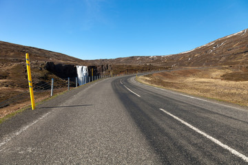 Human and nature: clean water of waterfall and asphalt road on a stony rocky mountain landscape of Iceland