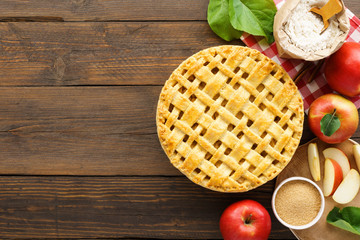 Apple pie with lattice top and ingredients on wooden table.