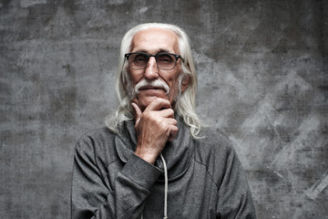 Aged gray haired Caucasian retired man thinking about life. Grandfather in glasses with mustache and thoughtful facial expression holds his chin