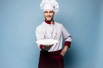 Portrait of a happy male chef cook standing with plate isolated on light blue background.