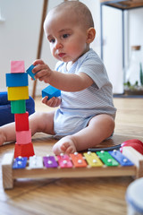 Mother With 8 Month Baby Son Learning Through Playing With Coloured Wooden Blocks At Home
