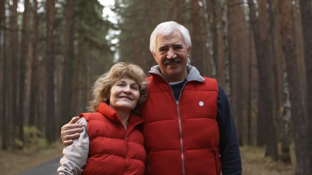 Medium shot of senior man and woman in sportswear standing together in woods