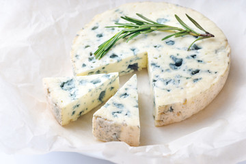 Slice of tasty blue cheese with rosemary on paper background