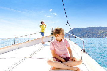 Two little kid boys, best friends enjoying sailing boat trip. Family vacations on ocean or sea on sunny day. Children smiling. Brothers, schoolchilden, siblings, best friends having fun on yacht.