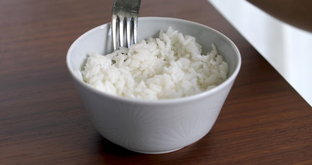 Closeup of woman eating rice from bowl with fork