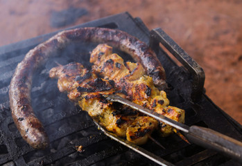 Barbecue - turning sausage and chicken skewers on a metallic grid