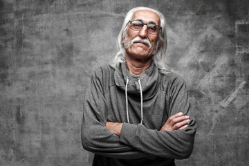 Old Caucasian gray-haired cool grandfather with glasses incredulously looks into the camera with crossed arms and serious face with copy space in studio