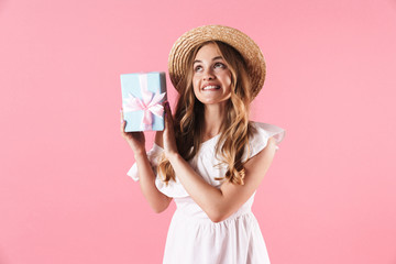 Image of thinking dreamy woman wearing straw hat looking upward and holding present box
