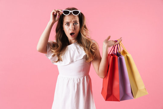 Image of beautiful shocked woman wearing white dress holding shopping bags and sunglasses