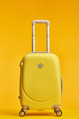 yellow travel bag with handle and wheels isolated on orange
