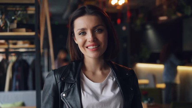 Portrait of good-looking young woman happy brunette in cafe smiling laughing looking at camera. Girl is wearing trendy leather jacket and white T-shirt.