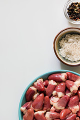 Fresh raw chicken hearts on light background. Offals on plate and spices for cooking. Top view, vertical, copy space.