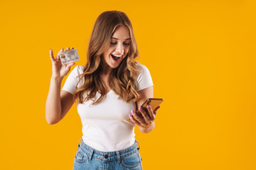 Photo of amazed young woman rejoicing while holding credit card and smartphone
