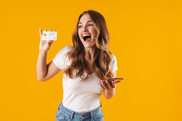 Photo of delighted young woman rejoicing while holding credit card and smartphone